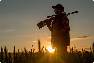 A woman holding a rifle in a field at sunset
