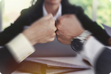 Two business professionals fist bumping, symbolizing teamwork and success in the competitive world of gun trust strategies. - Alex Kincaid Law
