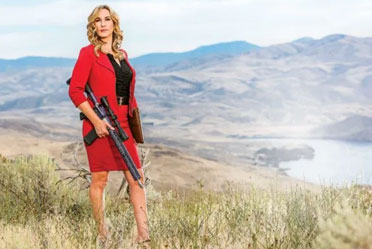 A woman in a red suit holding a gun in the mountains.