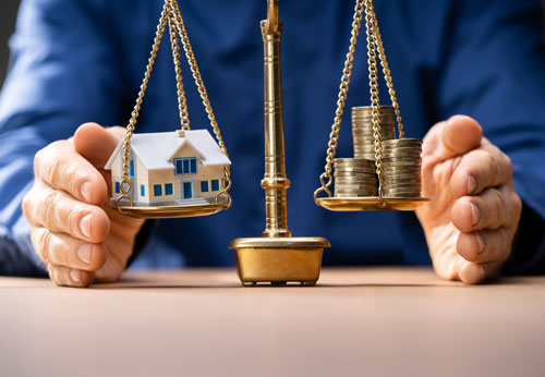 Scales of justice balancing a house and stacks of coins.