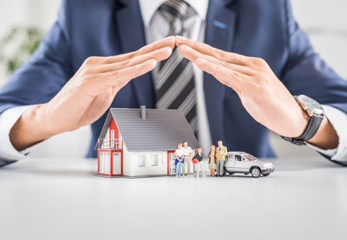 Hand sheltering piggy bank, paper houses, and wooden figures: asset protection.
