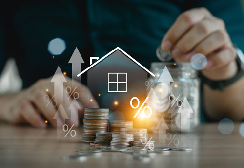 Close-up of hands, a stack of coins, and a house icon, symbolizing property investment and financial growth.